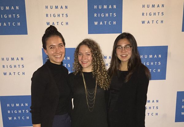 Three young, well-dressed women in front of a Human Rights Watch banner