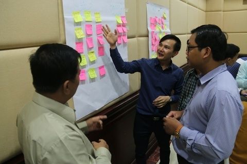 Cambodian professors stand by a paper hanging on a wall covered in post-its as they workshop interactive teaching methodologies.